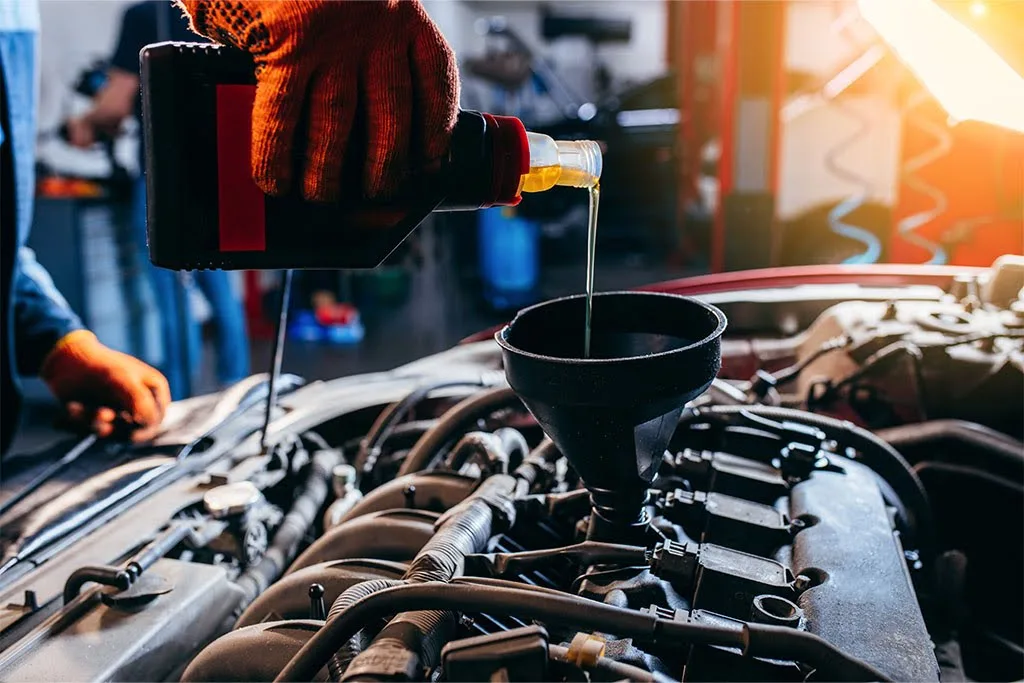 a mechanic pouring engine oil into the engine of a car using a funnel